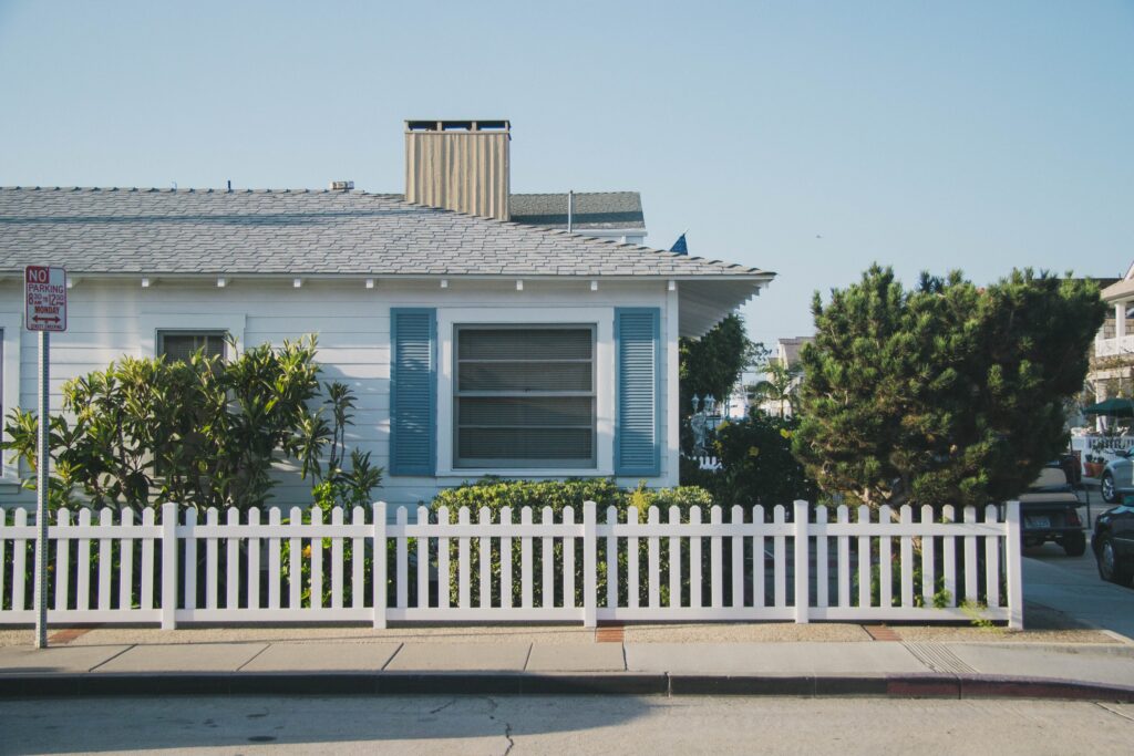 White house with blue shutters on a corner with a white fence
