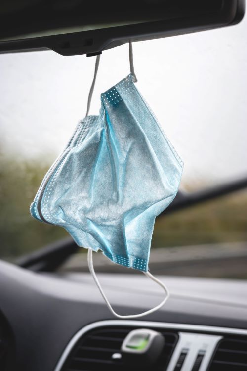 disposable face mask hanging off of a car's rearview mirror