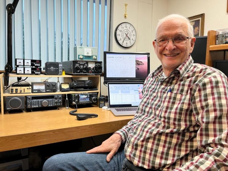 a man smiling at the camera with his ham radio set up behind him