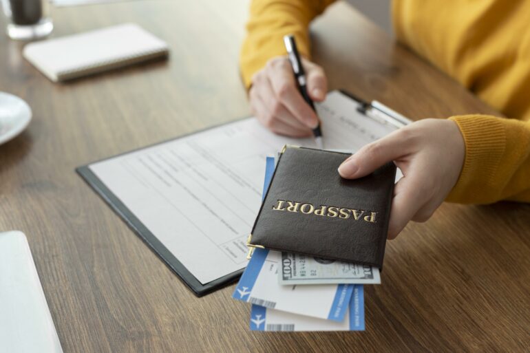 A passport with tickets slotted inside, in one hand, and person is filling out forms with the other.
